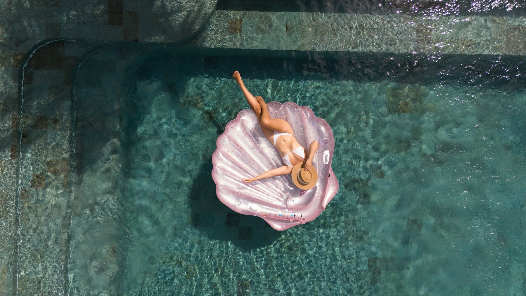 Aerial view of the infinity pool at Oshom Bali, guest floating on a pink pool float