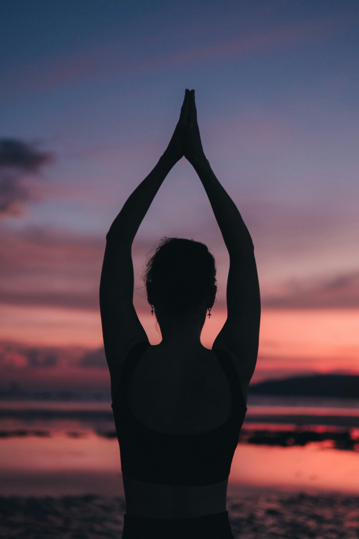 Woman meditating in prayer pose, sunset over the ocean
